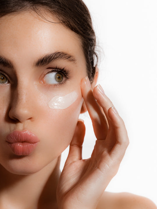 Woman applying cream under her eye on a white background